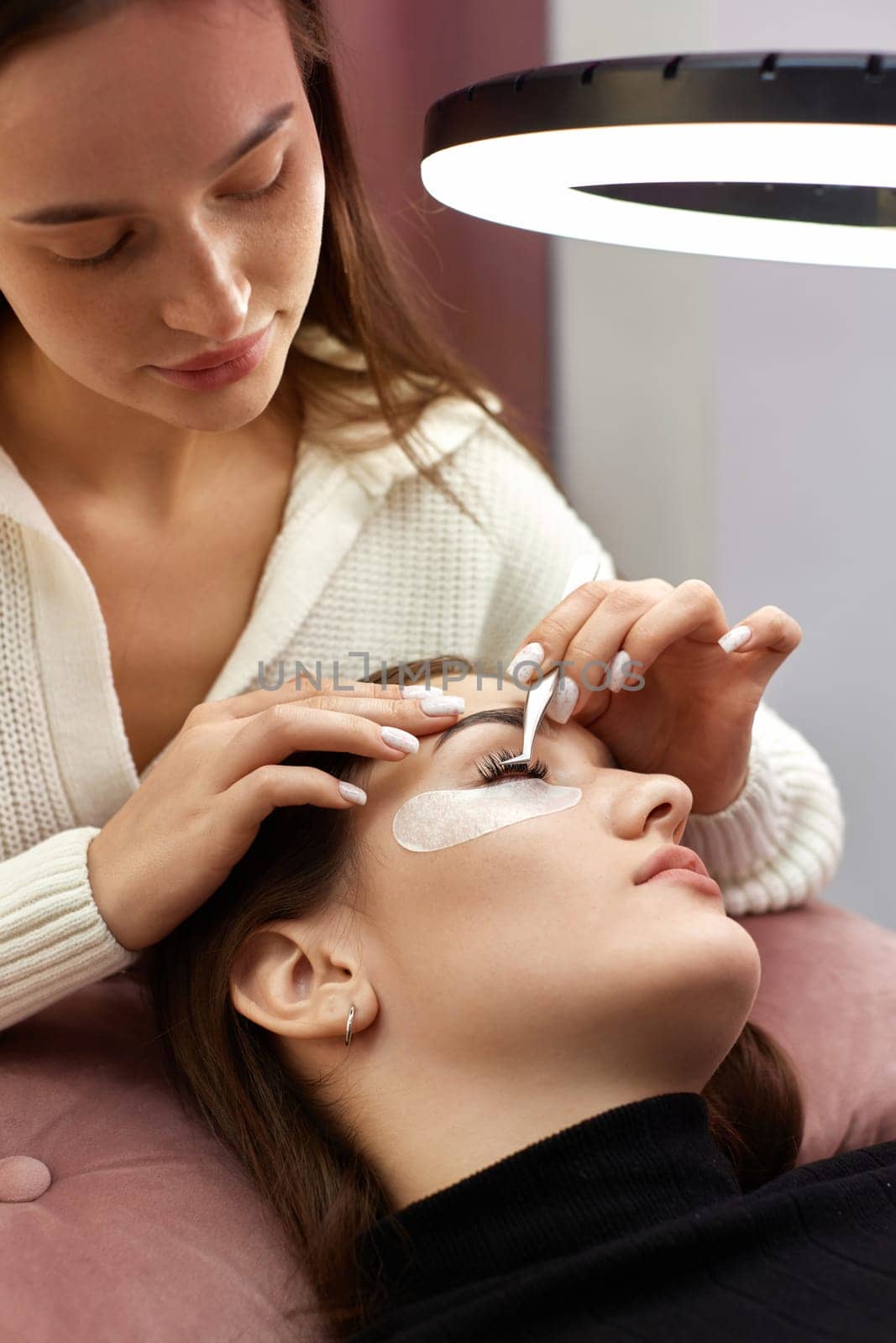 professional beautician with tweezers makes eyelash extension by erstudio