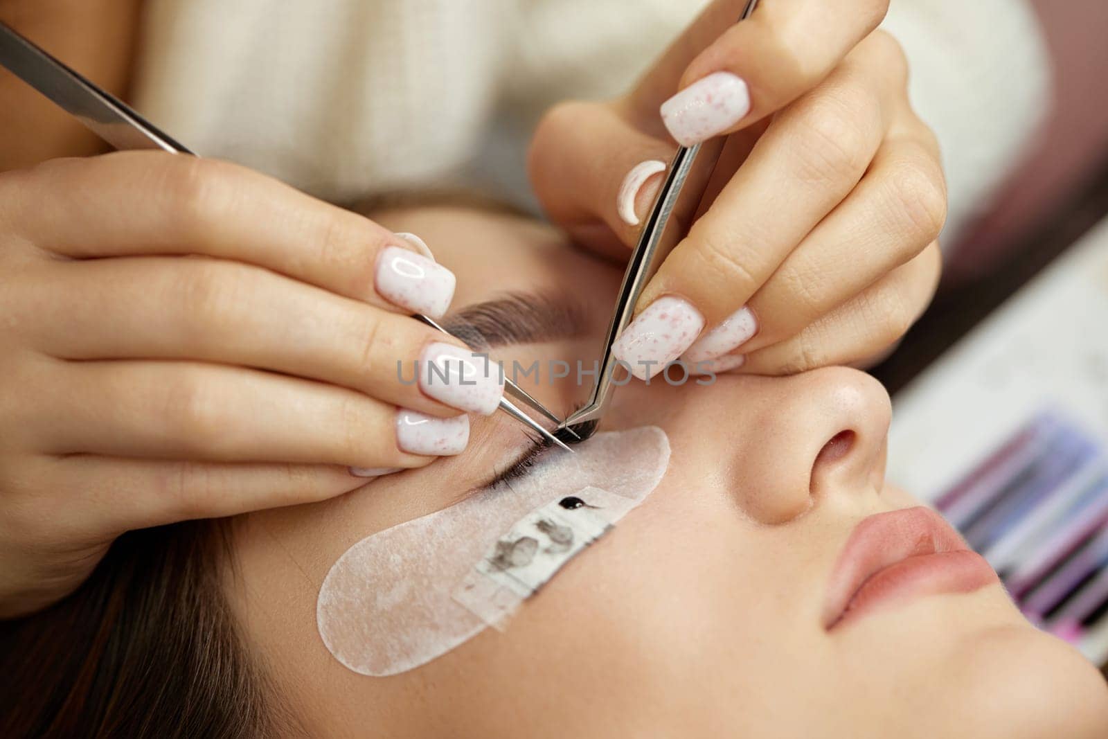 Beautiful female face during lash extension procedure in salon. Fake eyelashes