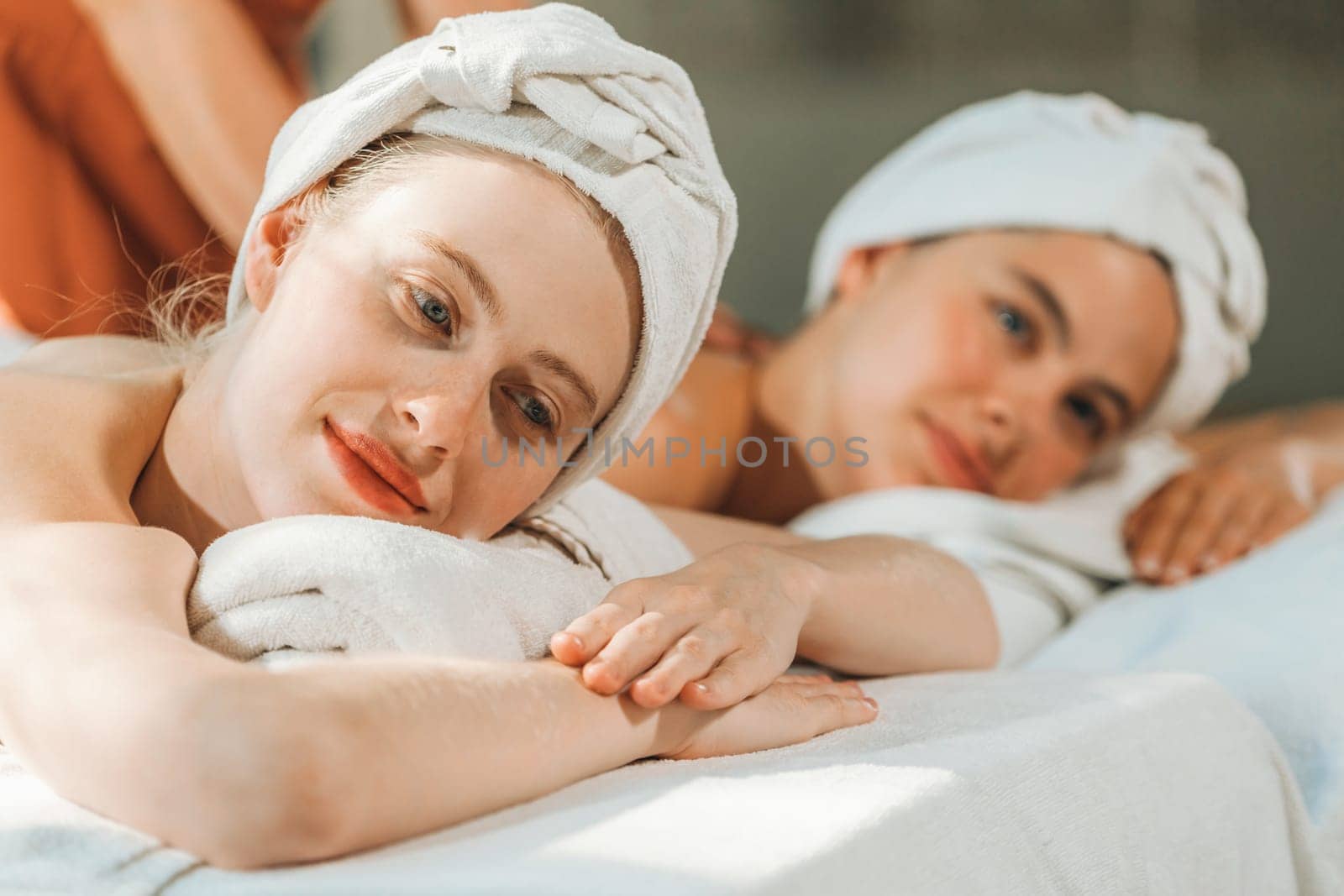 A couple of beautiful young woman lie on comfortable spa bed. Tranquility. by biancoblue