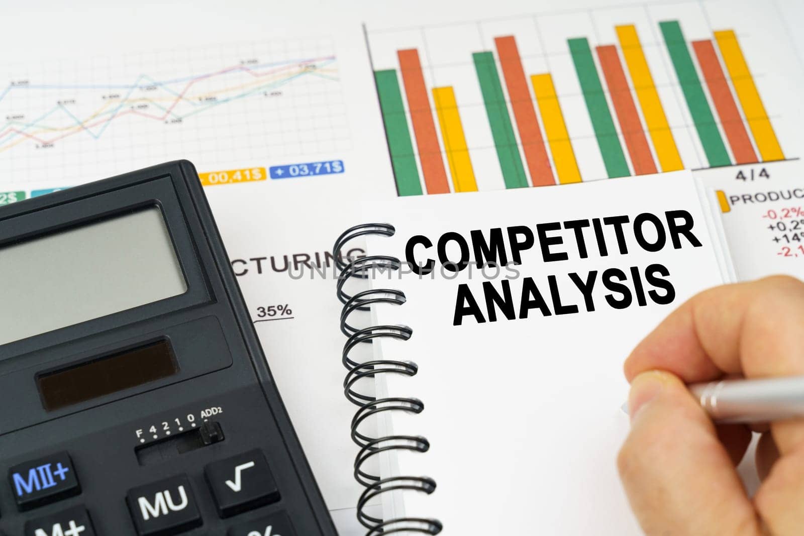 Business concept. There is a calculator on the table, business charts, a man made a note in a notebook - Competitor Analysis