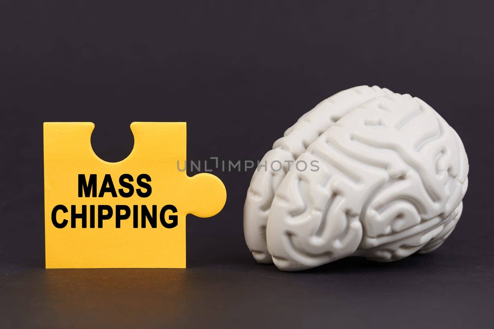 On a black surface there is a brain and a yellow puzzle with the inscription - mass chipping. Science and technology concept.