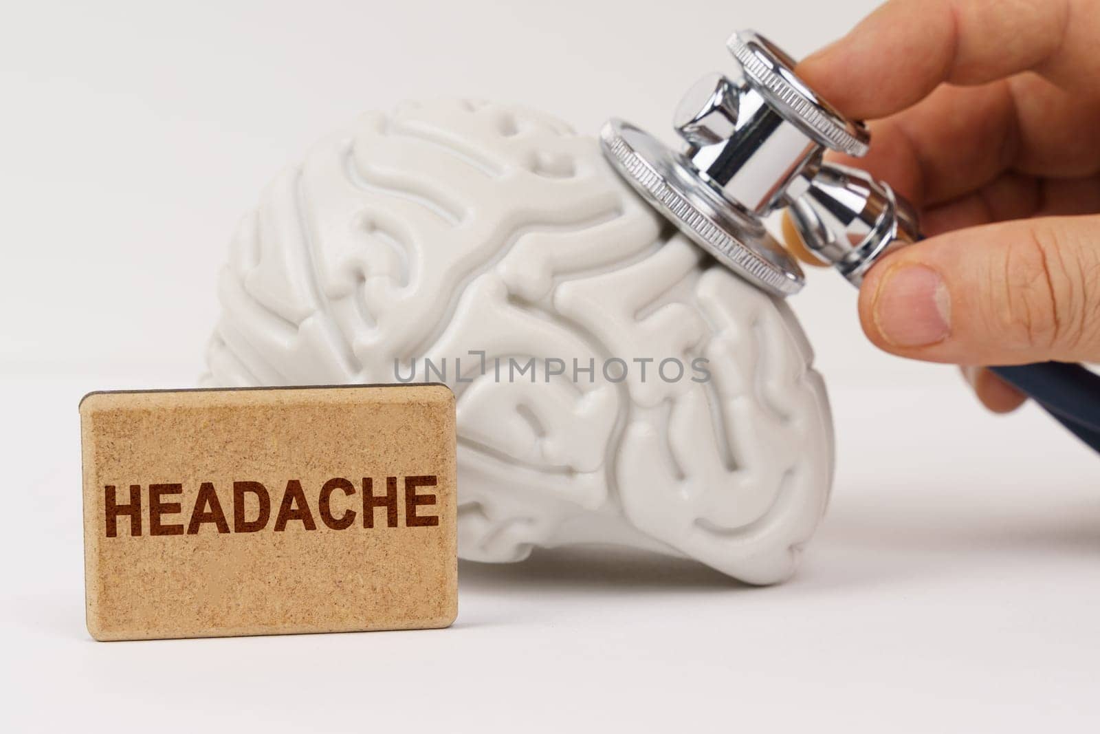 Medical concept. On a white surface, the brain is diagnosed using a stethoscope, next to it is a sign with the inscription - Headache