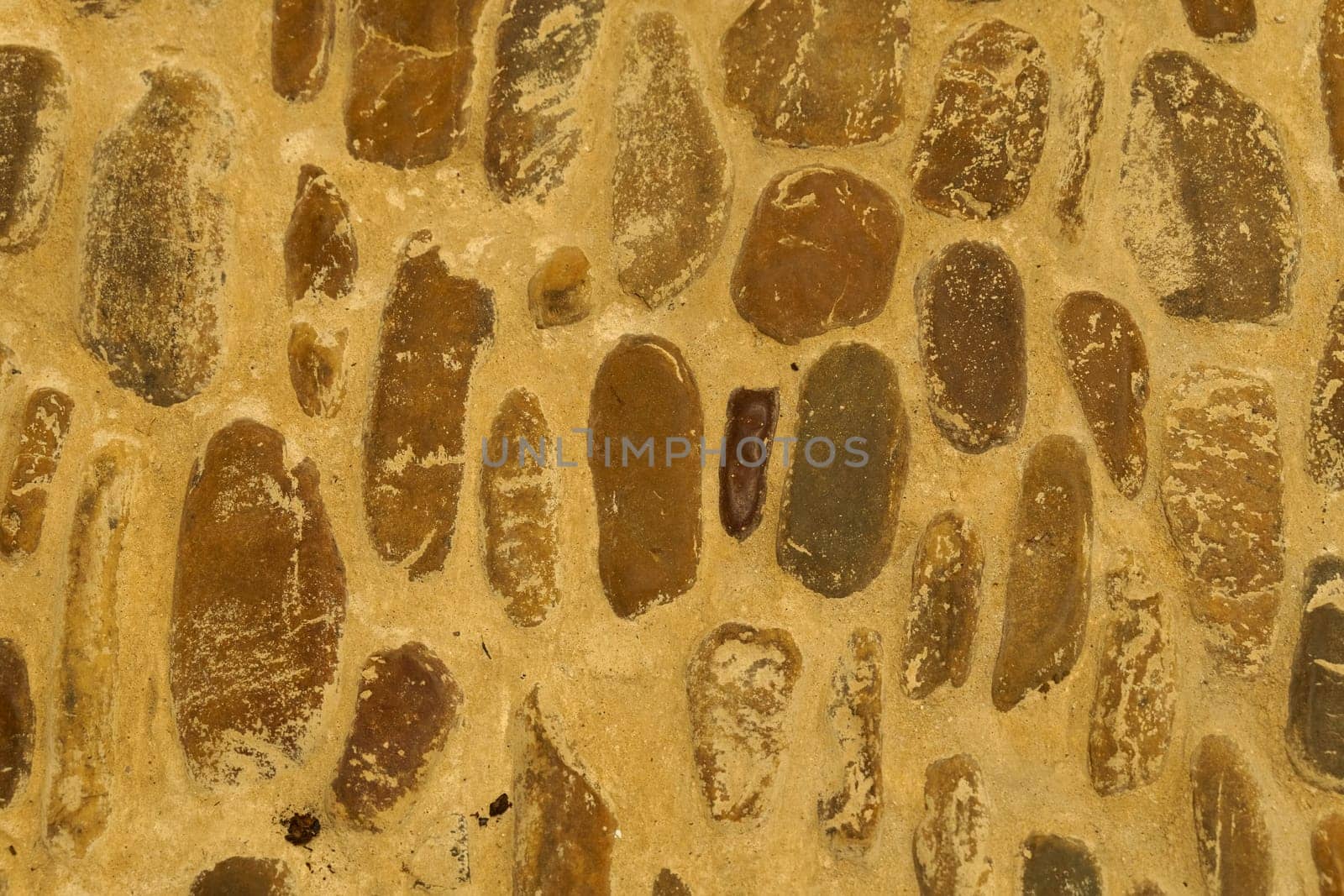 Old rough stone wall made of various square natural stones in beige, gray and brown colors. Construction texture.