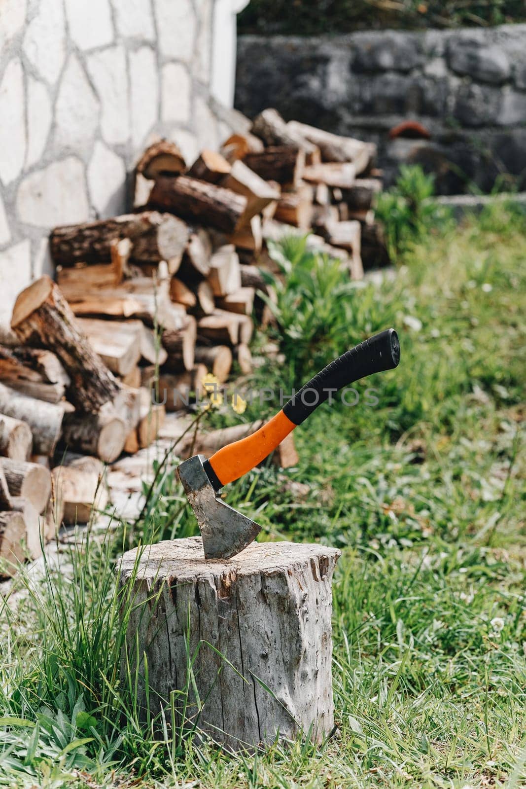 Axe with orange handle for the crib logs sticks sticking out in the tree amid the lie wood and green grass