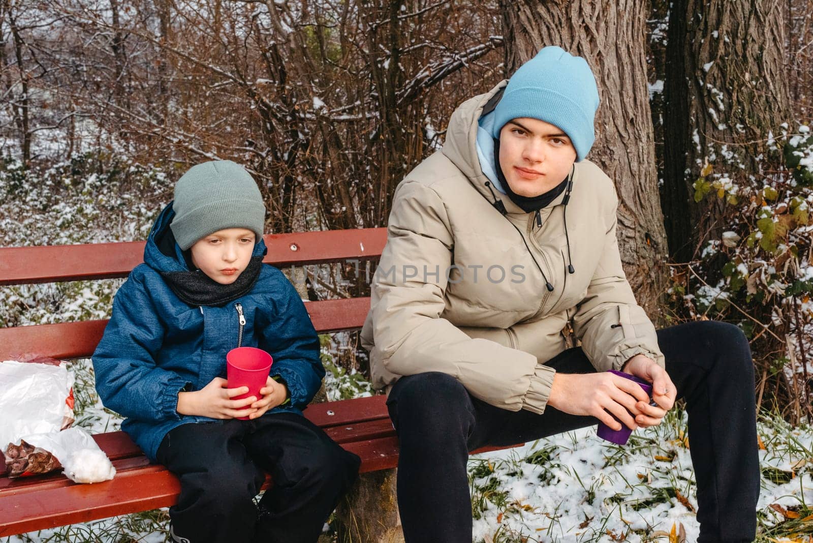 Snowy Park Serenity: Sons Share Treats and Smiles in a Winter Wonderland. Winter's Togetherness: A Delightful Bench Picnic with the Boys. A Heartwarming Winter Picnic with Father and Sons in a Snow-Kissed Park by Andrii_Ko