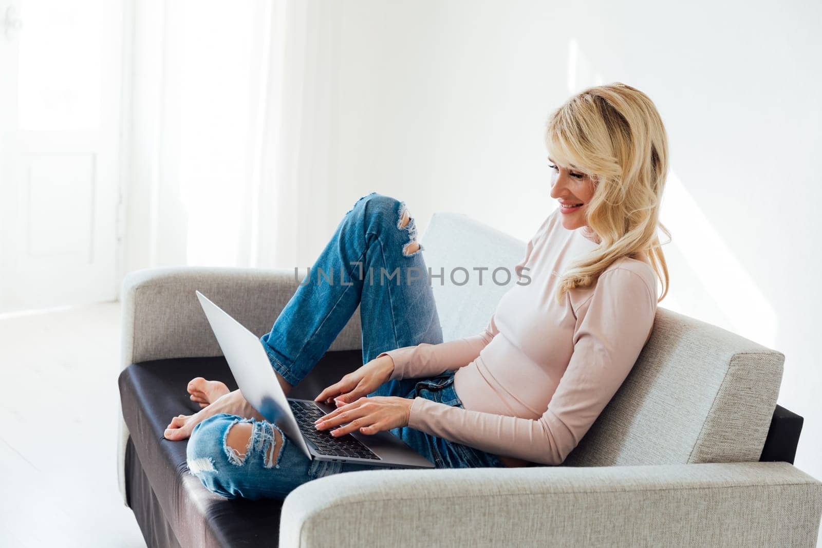 Blonde woman working on laptop on couch small business online by Simakov