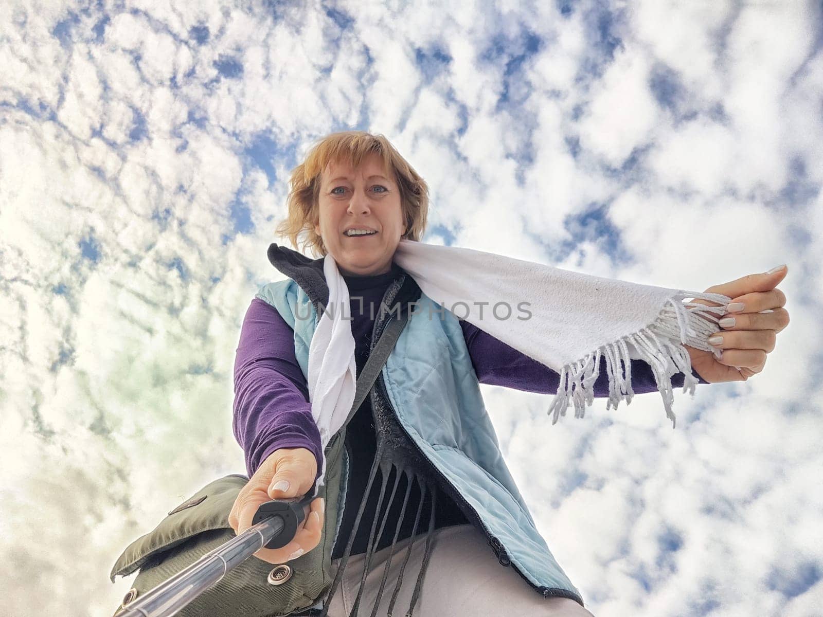 A happy, funny, funny adult girl takes a selfie against a blue sky with white clouds. A middle-aged woman poses on the phone in nature in autumn or spring by keleny