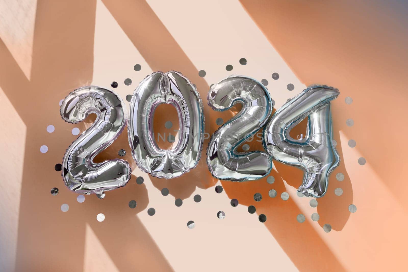 Silver numbers 2024 new year balloons among confetti in sunlight on Peach Fuzz background Happy new year celebration party. Greetings and congratulation color of the year 2024 pantone