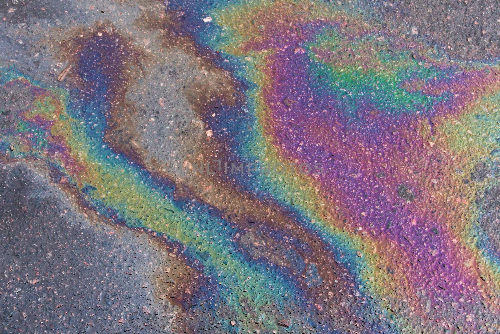 Colored texture of oil products on the asphalt in the rain. Oil dripped from the car engine onto the road.