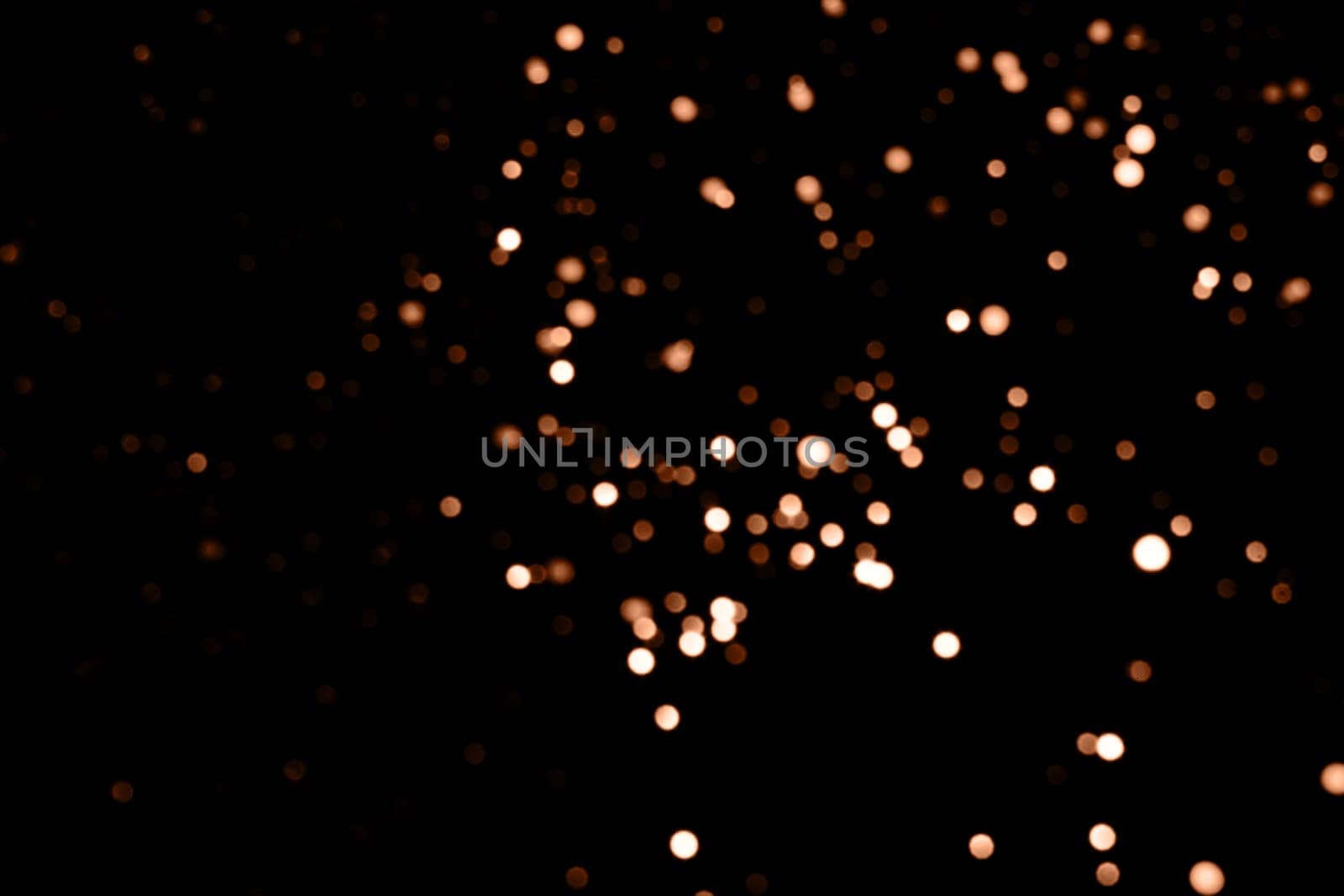 Blurry garland lights on a dark background. Festive Christmas and New Year background. Soft focus. Image toned in color of the year 2024 - Peach Fuzz.