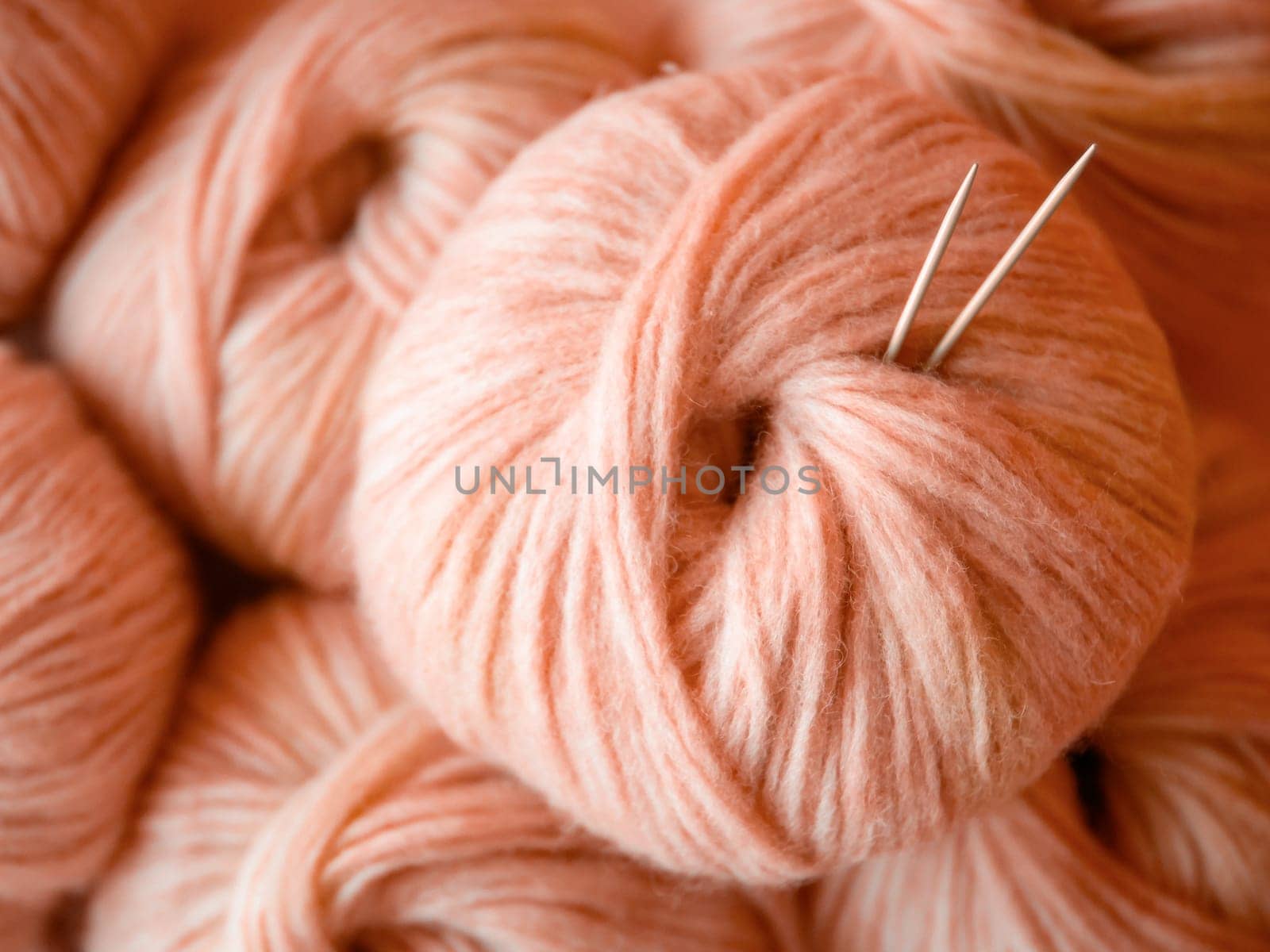 Aesthetic image of Peach Fuzz color beige of year, airy yarn skein. Close up view of medium thick blow yarn made of baby alpaca and merino wool. Knitting needles stuck in skein of yarn. Copy space