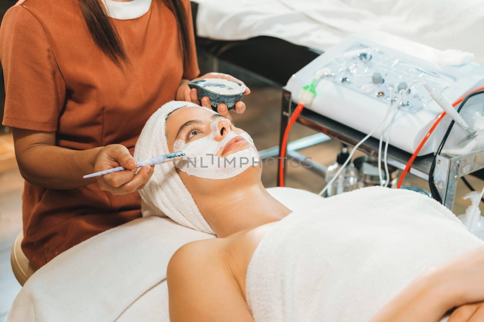 Beautiful young women lie on spa bed while having facial massage from professional doctor. Attractive female with beautiful skin surrounded by electric facial machine. Tranquility.