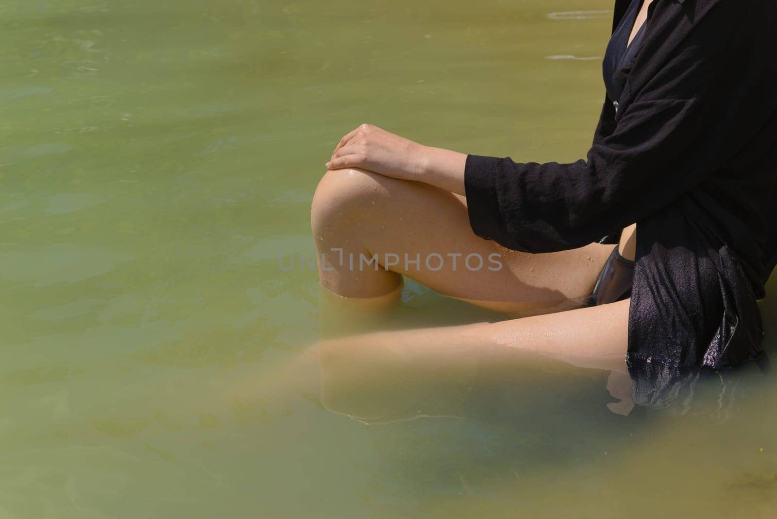 Part of the body, leg and arm of a young woman in a dark dress sitting in the water. Selective focus