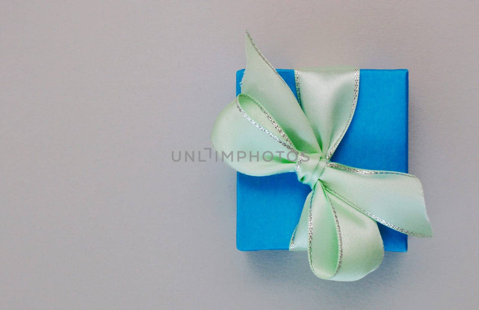 Gift box tied with satin pale green ribbon on a light gray paper background. copy space, place for text,