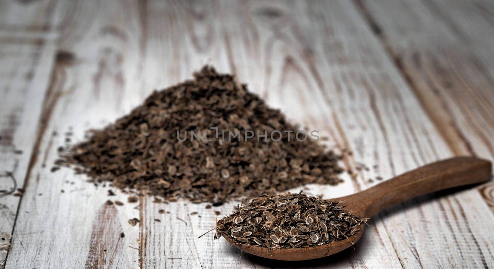 Natural wooden background with a spoon and a pile of dried dill seeds. Plant, food and medical themes. The concept of the usefulness of dill
