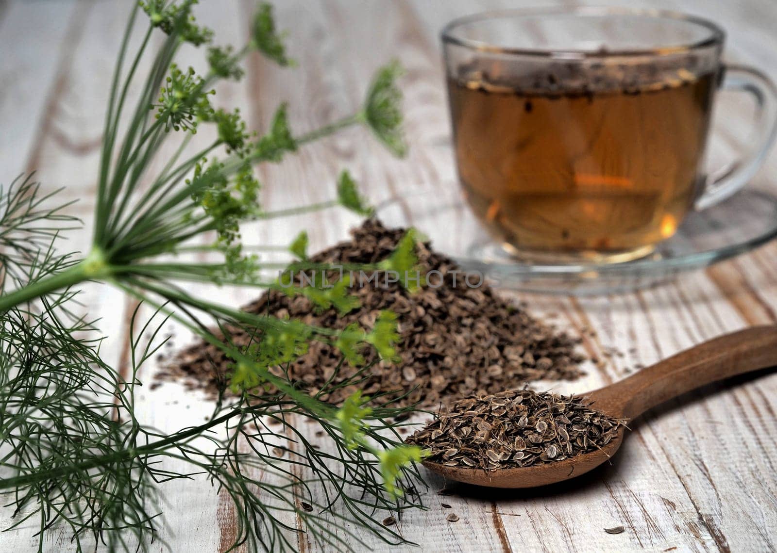 Medicinal tea with dried dill seeds in a cup and a pile of seeds on a natural wooden table. The concept of the usefulness of dill. by TatianaPink