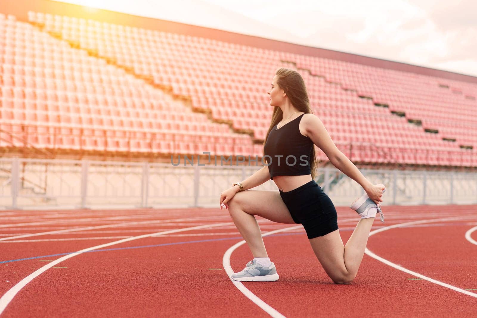 A female coach with dark hair stands on the red running track of the stadium, dressed in sports uniform.