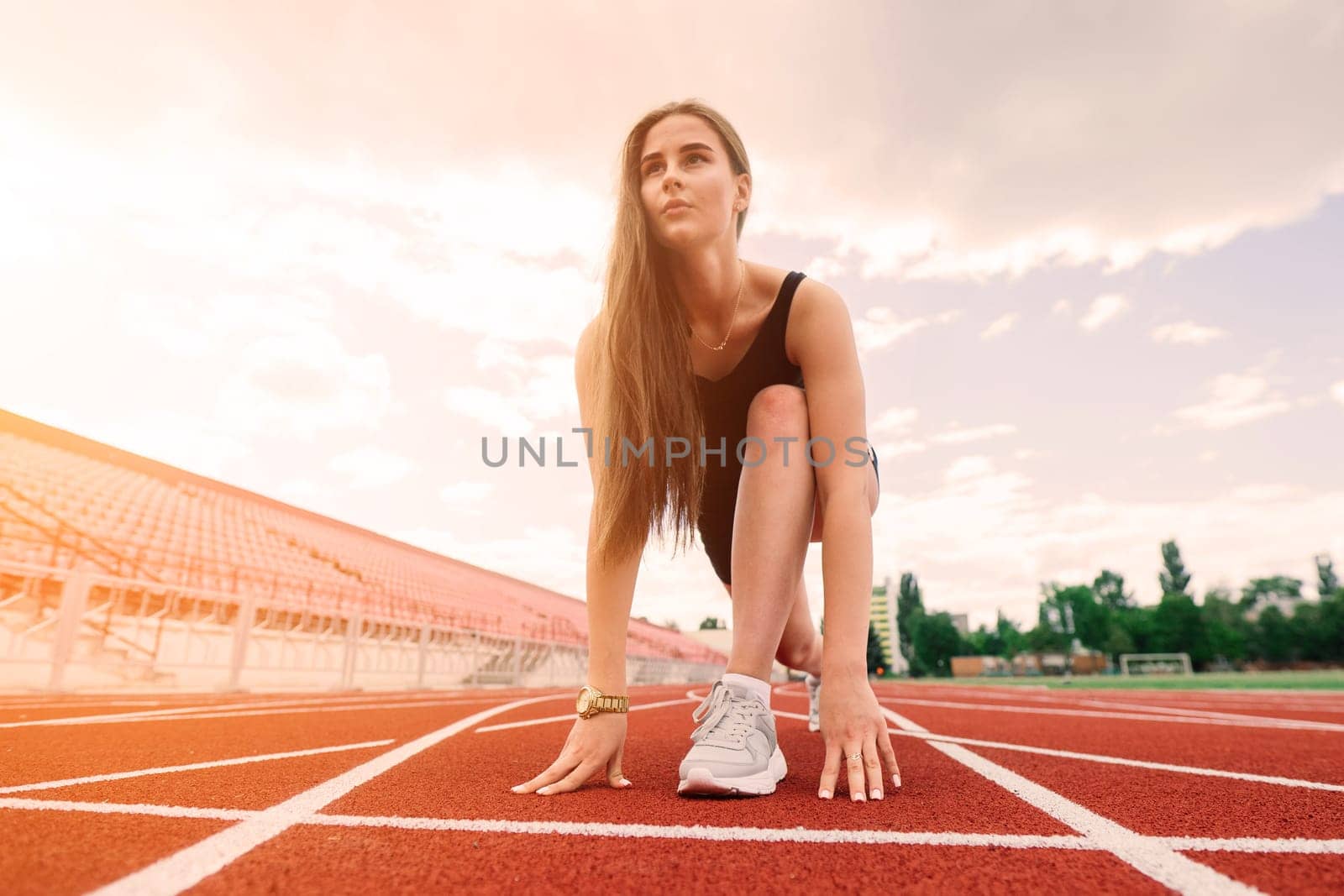 A female coach with dark hair stands on the red running track of the stadium, dressed in sports uniform.