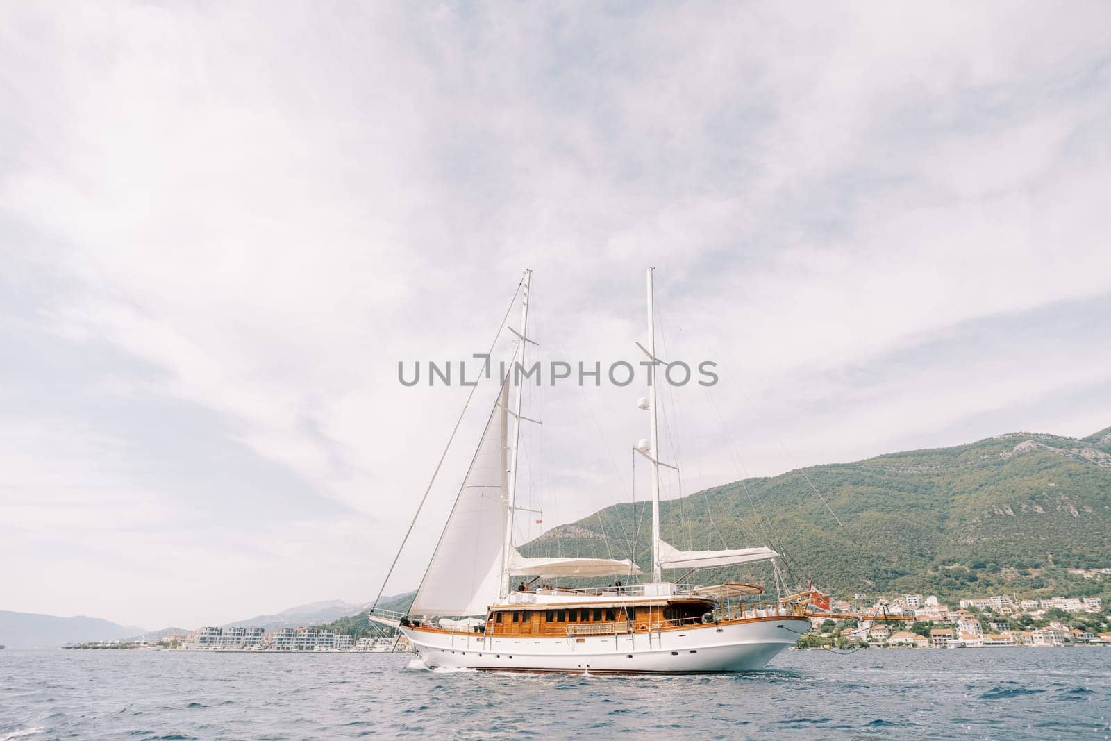 Luxury sailing yacht sails on the sea against the backdrop of green mountains. High quality photo