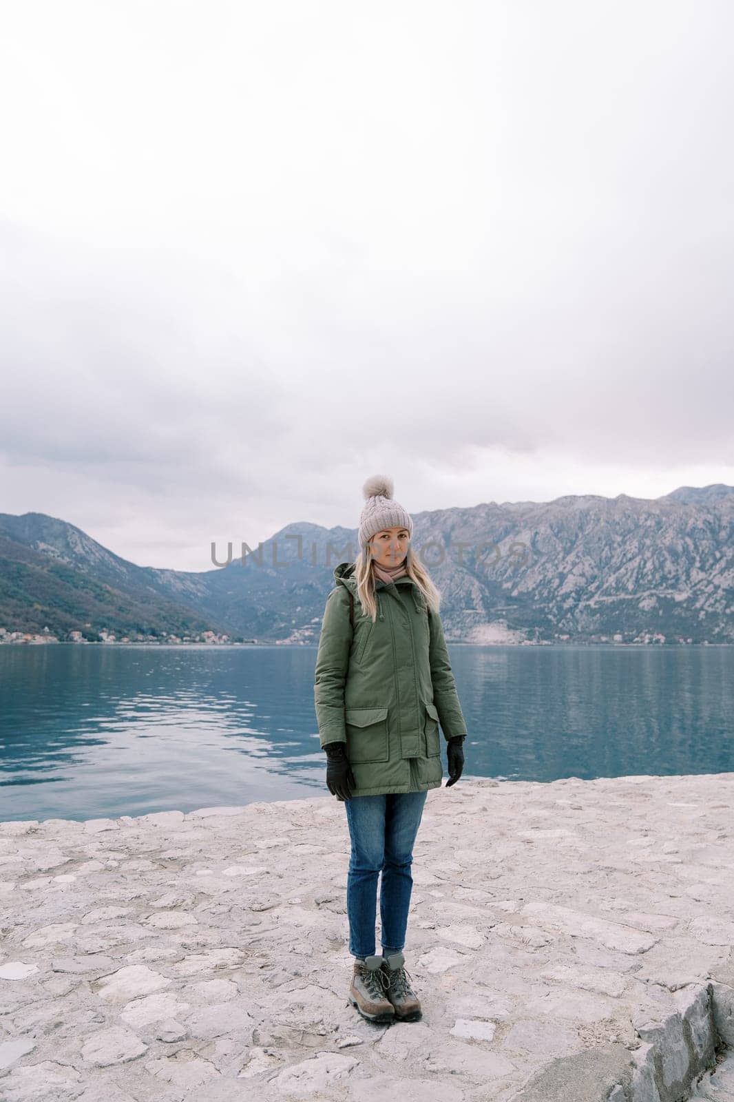 Young woman stands on a pier near the sea against the backdrop of mountains. High quality photo