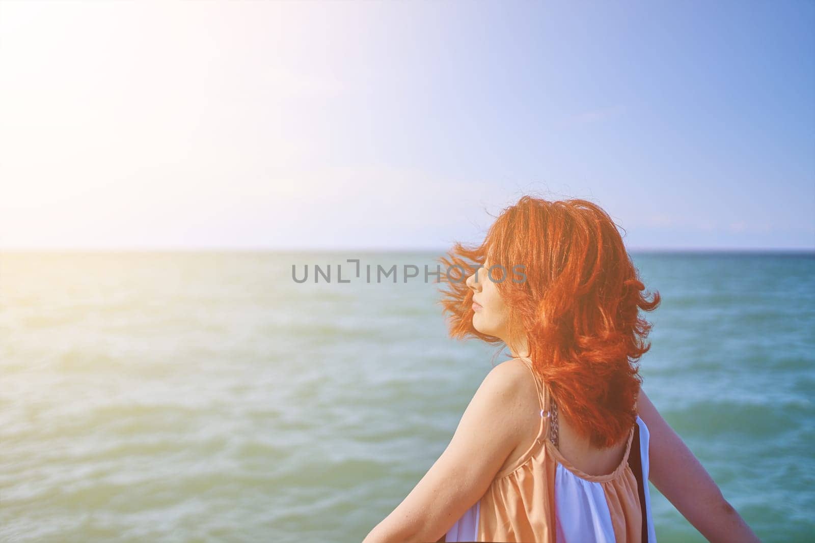 A serene beach setting illuminated by sunlight, featuring a young woman looking over her shoulder against the calming blue sea.