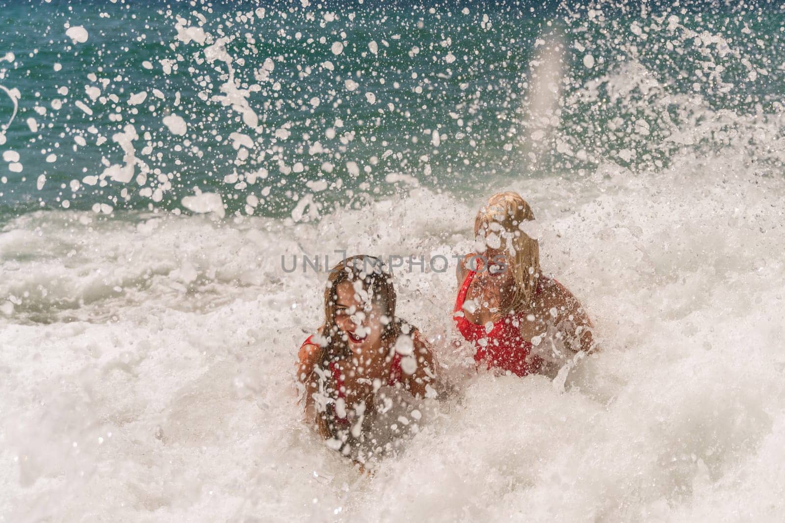 Women ocean play. Seaside, beach daytime, enjoying beach fun. Two women in red swimsuits enjoying themselves in the ocean waves