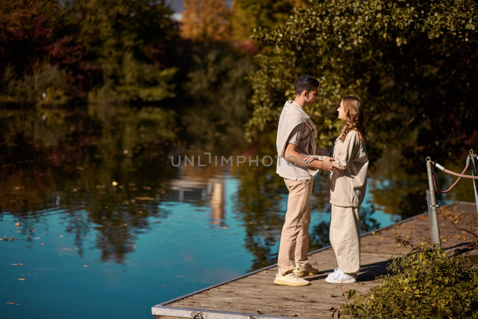 A happy couple in love in casual clothes travel together, hike and have fun in the fall forest on a weekend in nature in autumn outdoors, selective focus. COUPLE LOVE STORY park pond lake. Handsome man embracing with passion his girlfriend outdoor under the leaves of trees on the embankment. Love history. Happy people concept. by Andrii_Ko