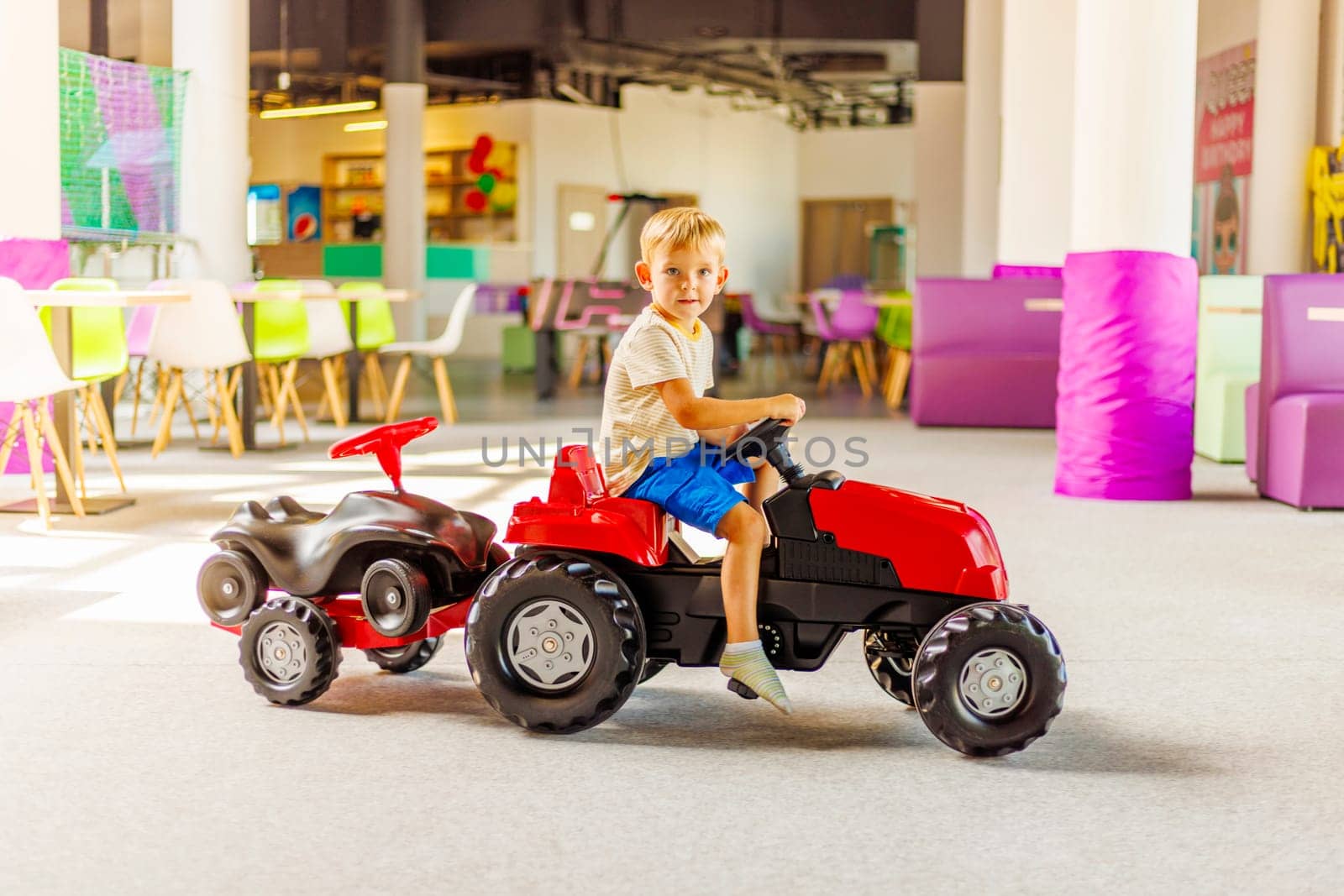 A child rides a toy pedal car at a children's play center by andreyz