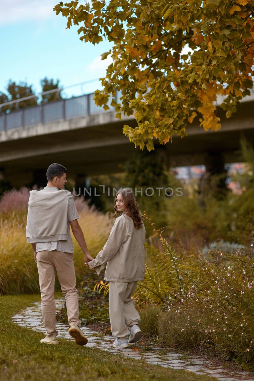 Young couple in love walking in the autumn park holding hands looking in the sunset. Closeup of loving couple holding hands while walking at sunset. The hands of the male and female lovers who hold hands walk forward high with blurred background
