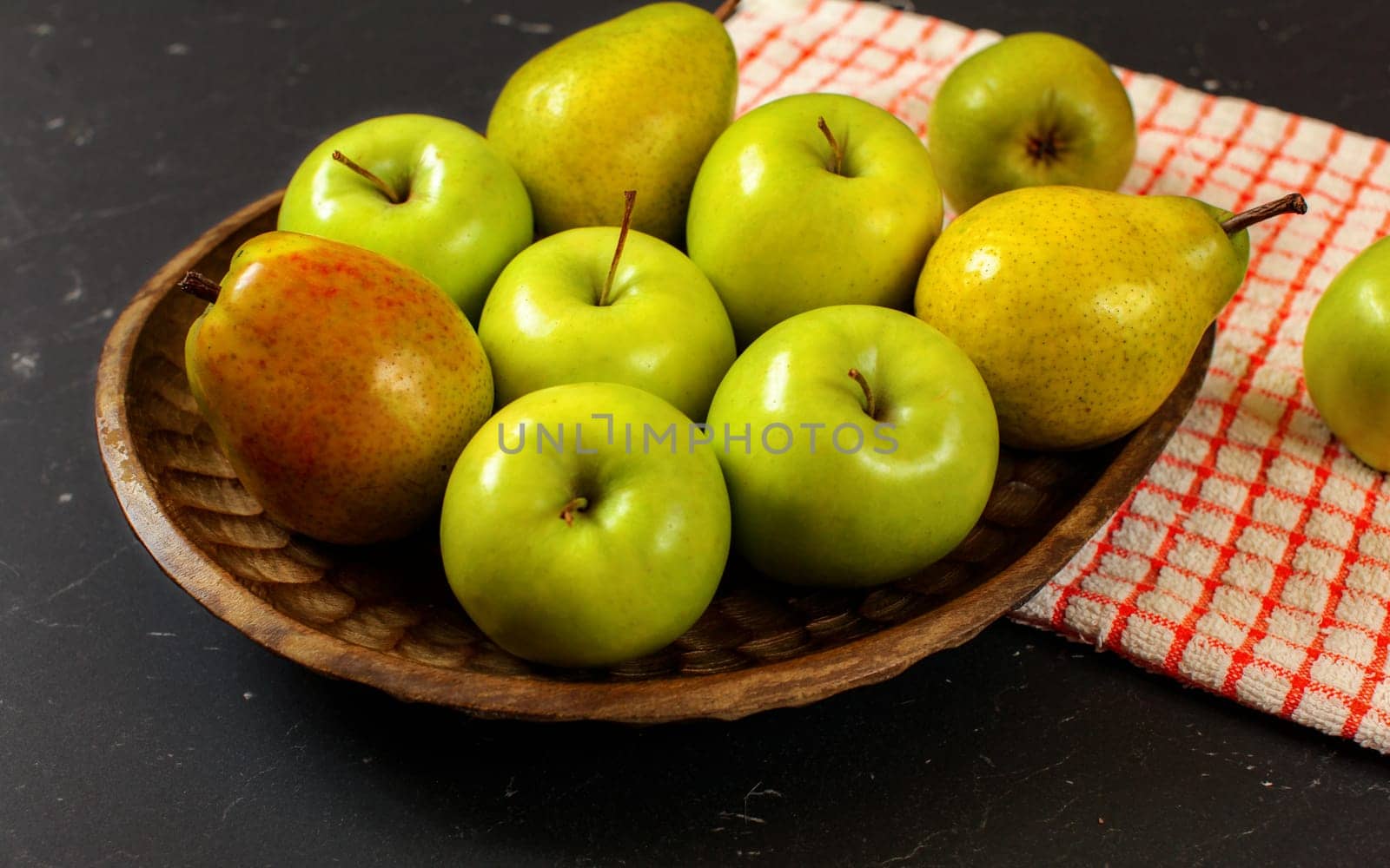 Wooden carved bowl with apples and pears with red chequered tablecloth on black board by Ivanko