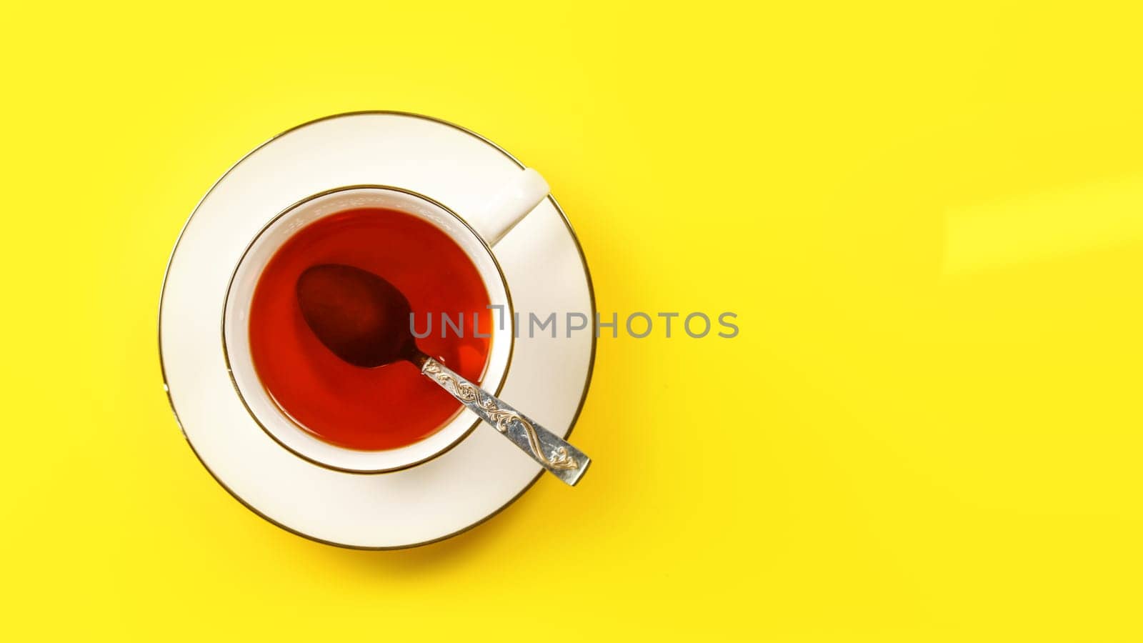 Flat lay photo, white porcelain cup of hot tea with silver spoon, on yellow board, space for text right