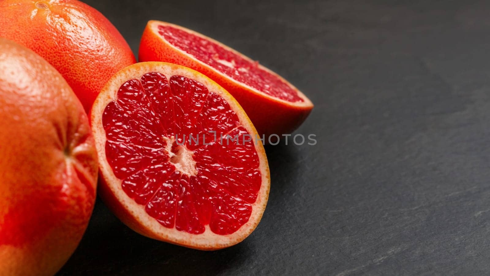 Pink grapefruits, one citrus halved, on black slate like board. by Ivanko