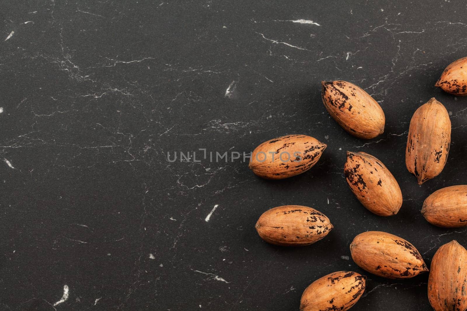 Whole pecan nuts on black marble like board, space for text left, overhead photo by Ivanko