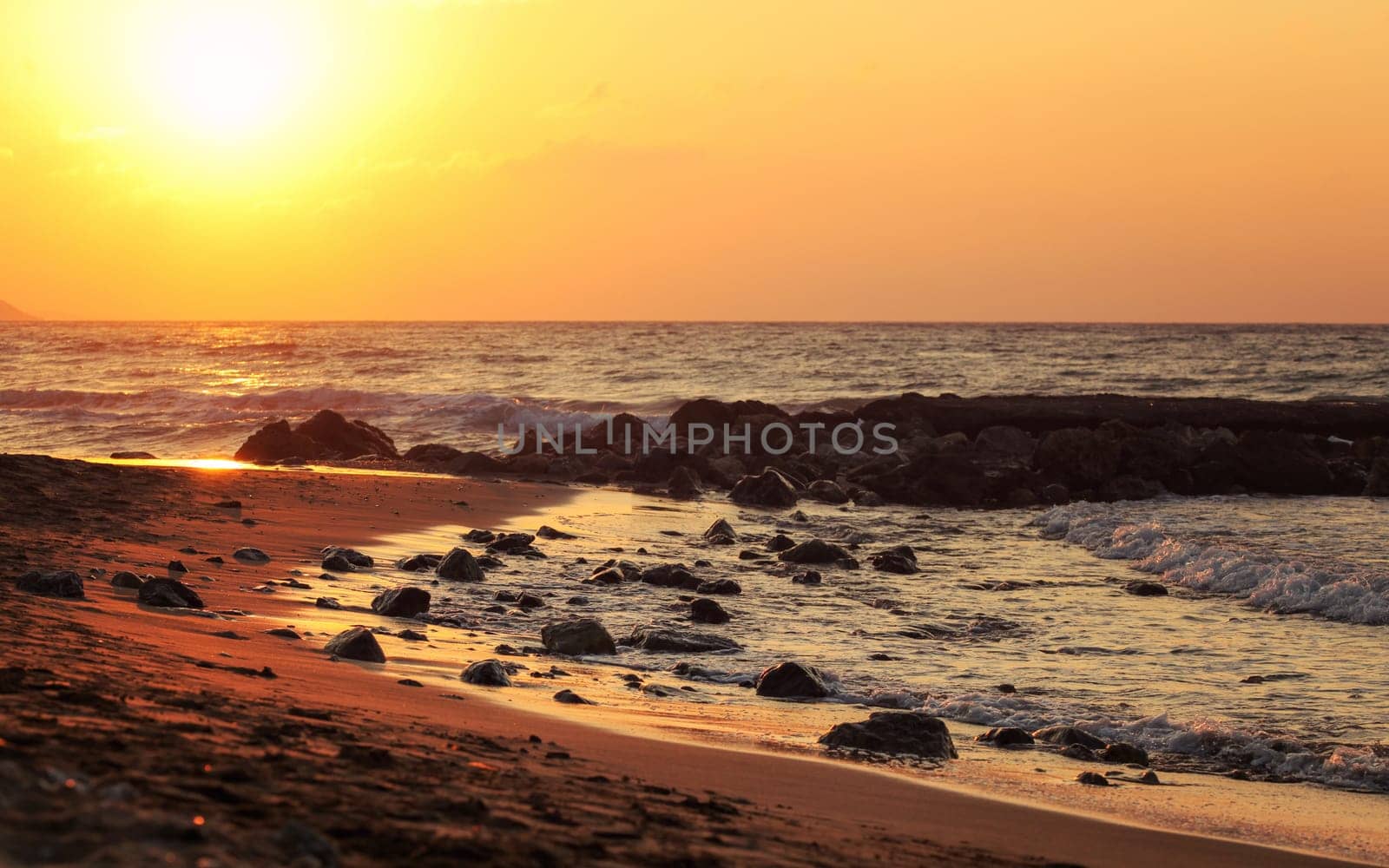 Sunset on wild beach, sun shines on wet stones in sand. by Ivanko