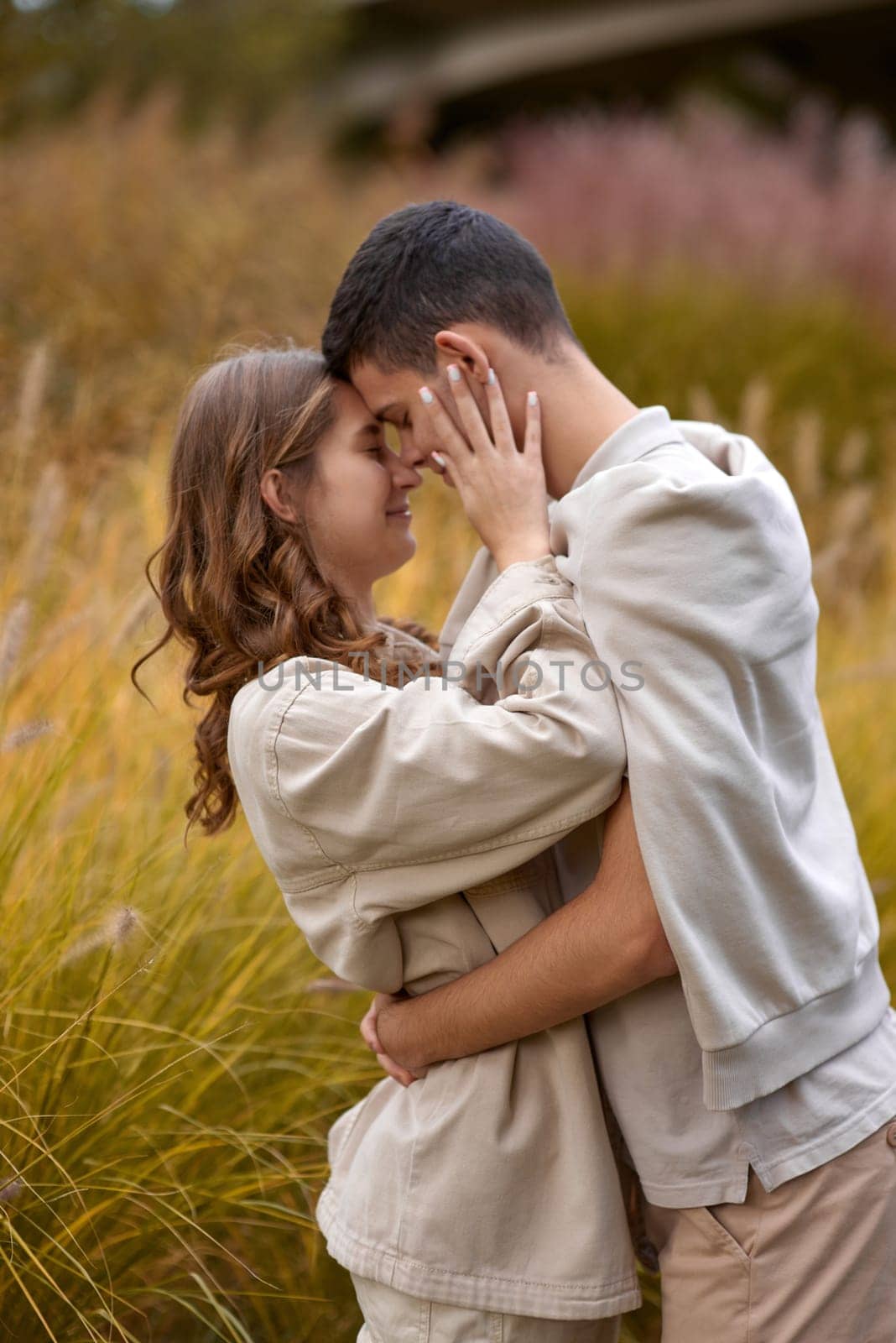 Happy couple on autumn walk outdoors. Two lovers in autumn park. Love and tender touch. Gentle hugs. Young man and woman in classic autumn colors outfit on a romantic date in a park. Young girl and guy with blond hair kisses, show love, affection. Boy and girl of European appearance with warm clothes, pictures with soft background bokeh blur fall. Concept of happiness,