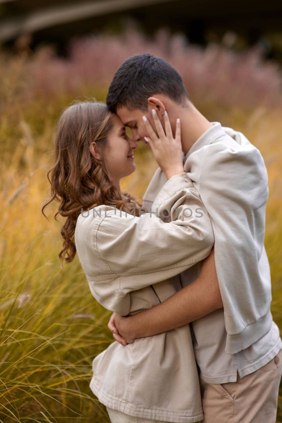 Happy couple on autumn walk outdoors. Two lovers in autumn park. Love and tender touch. Gentle hugs. Young man and woman in classic autumn colors outfit on a romantic date in a park. Young girl and guy with blond hair kisses, show love, affection. Boy and girl of European appearance with warm clothes, pictures with soft background bokeh blur fall. Concept of happiness,