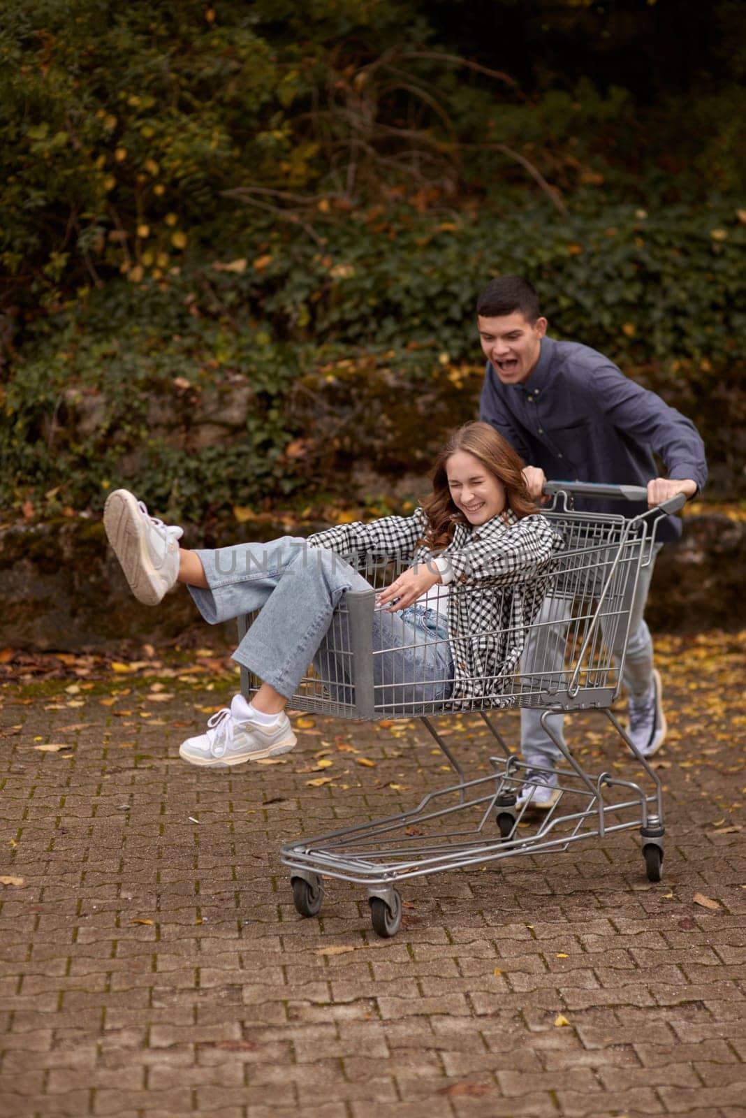 Autumn Joyride: Boy Rolling Girl in Shopping Cart amid Nature's Beauty. playful couple, autumnal adventure, outdoor fun, seasonal joy, laughter and love, romantic play, nature's embrace, joyful moments, couple goals, autumn magic.