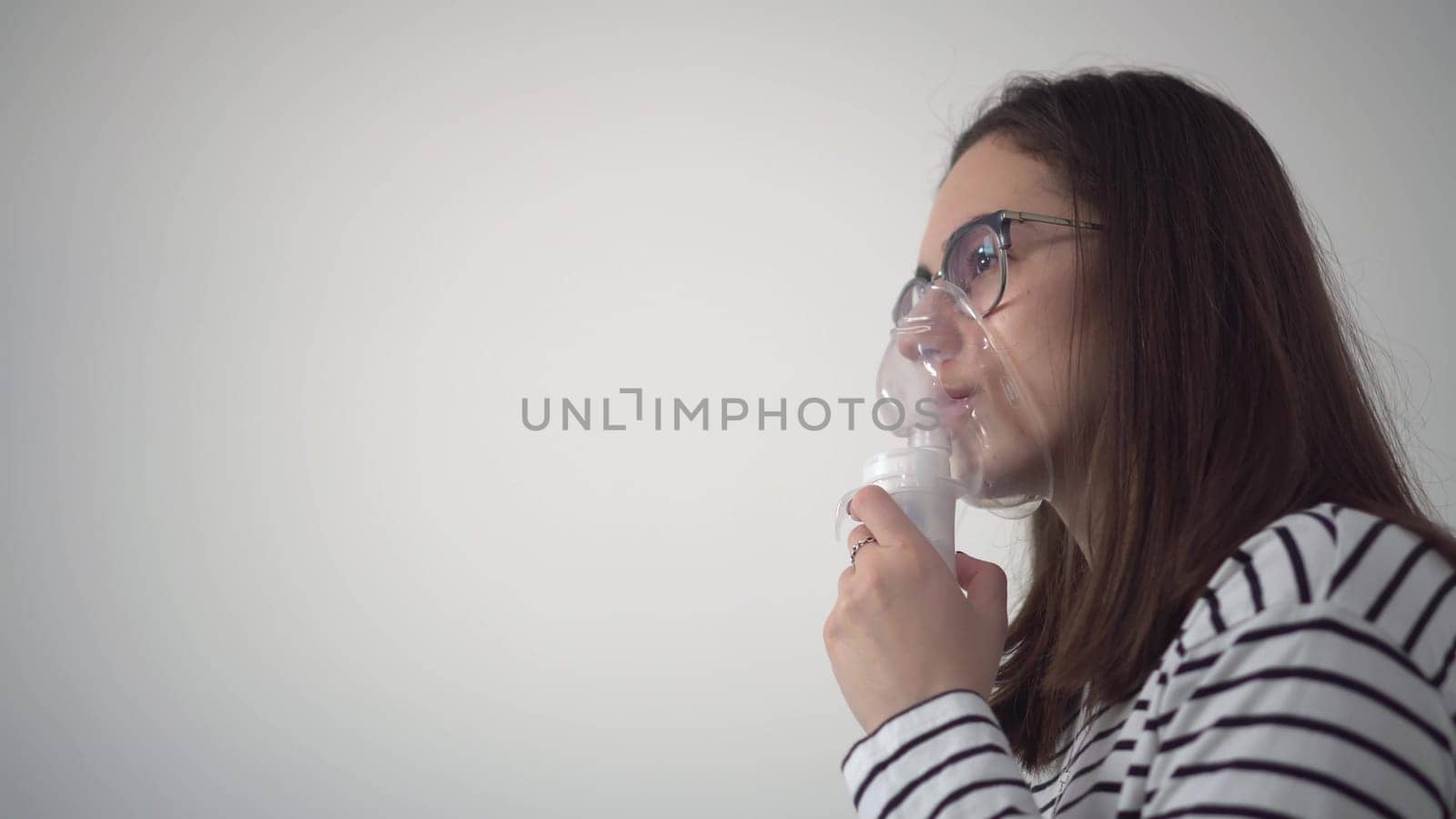 A young woman breathes through an inhaler mask closeup. A girl in glasses with an oxygen mask is being treated for a respiratory infection. 4k