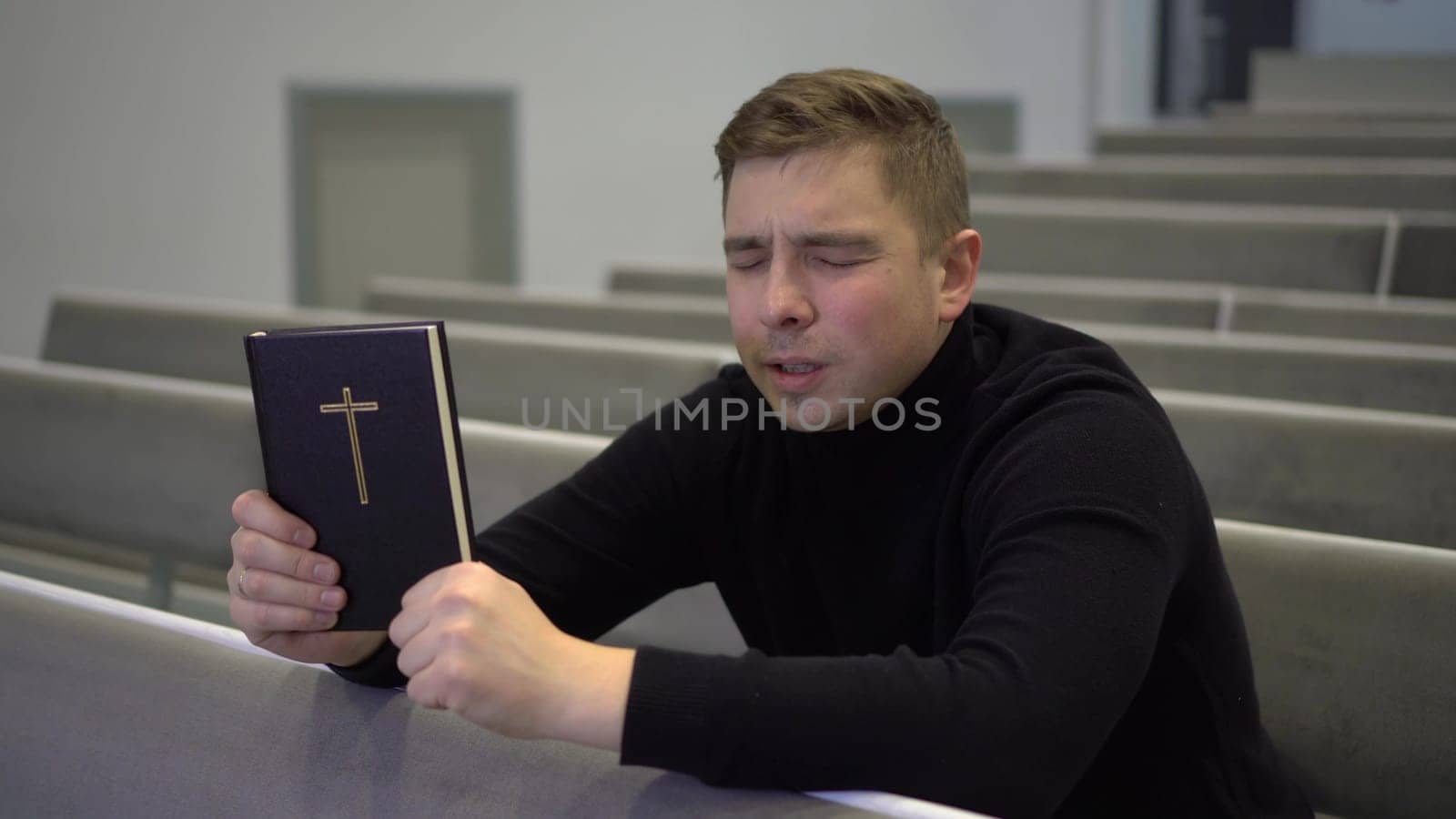 A young man prays holding a bible in his hands in a church. A Protestant man sits on a church bench and sincerely prays. 4k