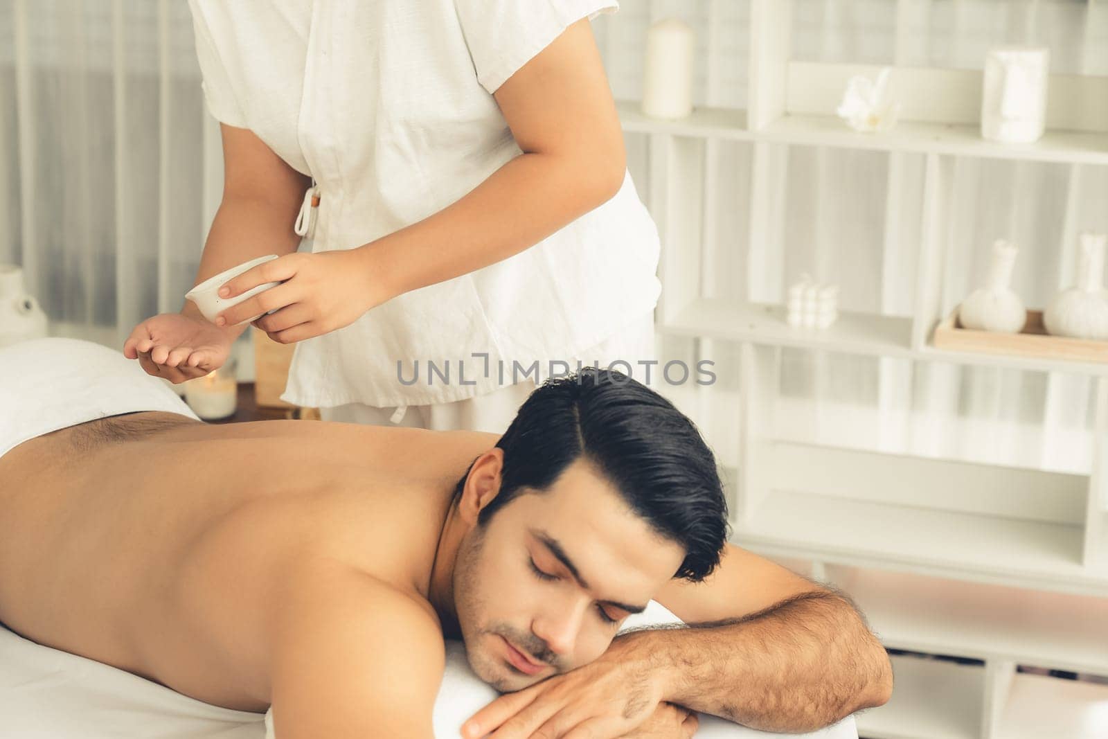 Caucasian man customer enjoying relaxing anti-stress spa massage and pampering with beauty skin recreation leisure in day light ambient salon spa at luxury resort or hotel. Quiescent