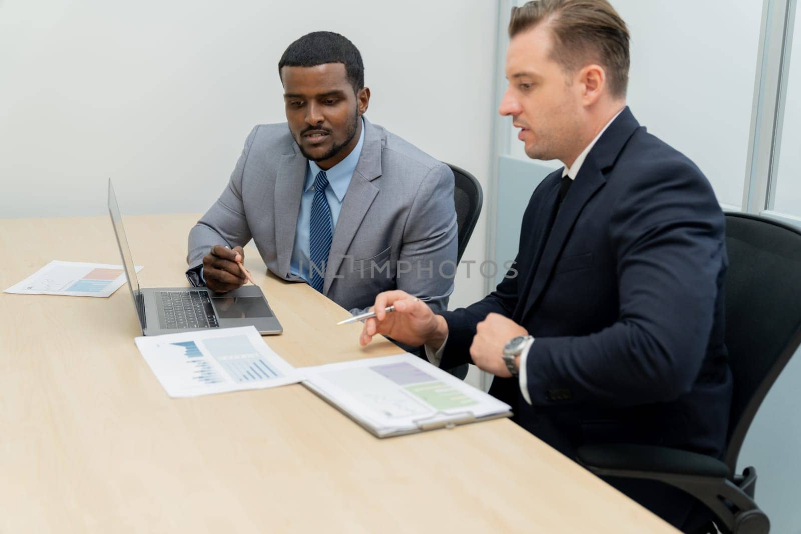 African male leader explain strategy while show solution to professional project manager by pointing at document, using laptop. Skilled business team brainstorming idea. Business meeting. Ornamented.