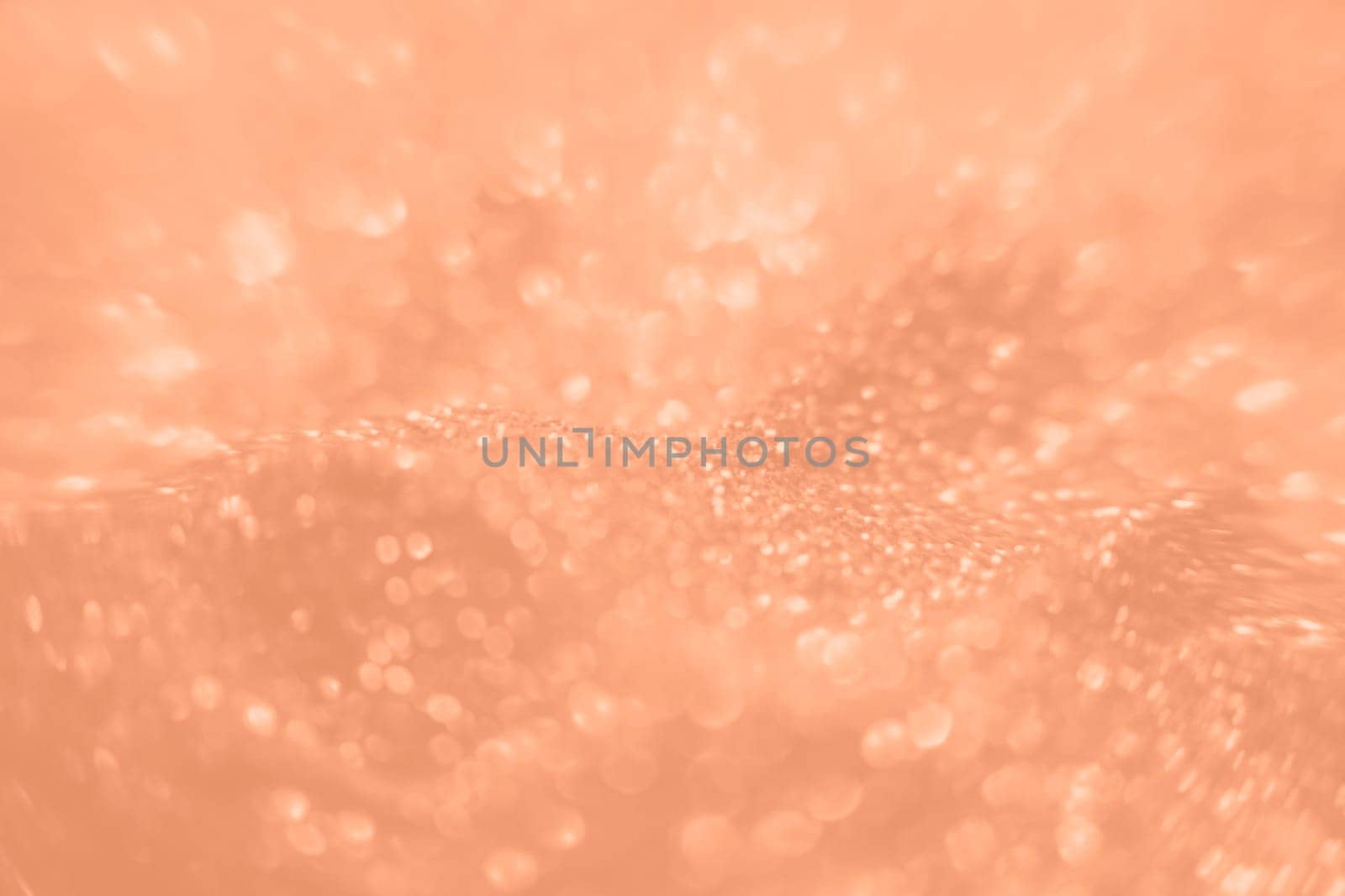 Peach Fuzz color glitter background. Blurred monochrome background with bokeh. Blurred glitters shimmering dust macro close up. High quality photo