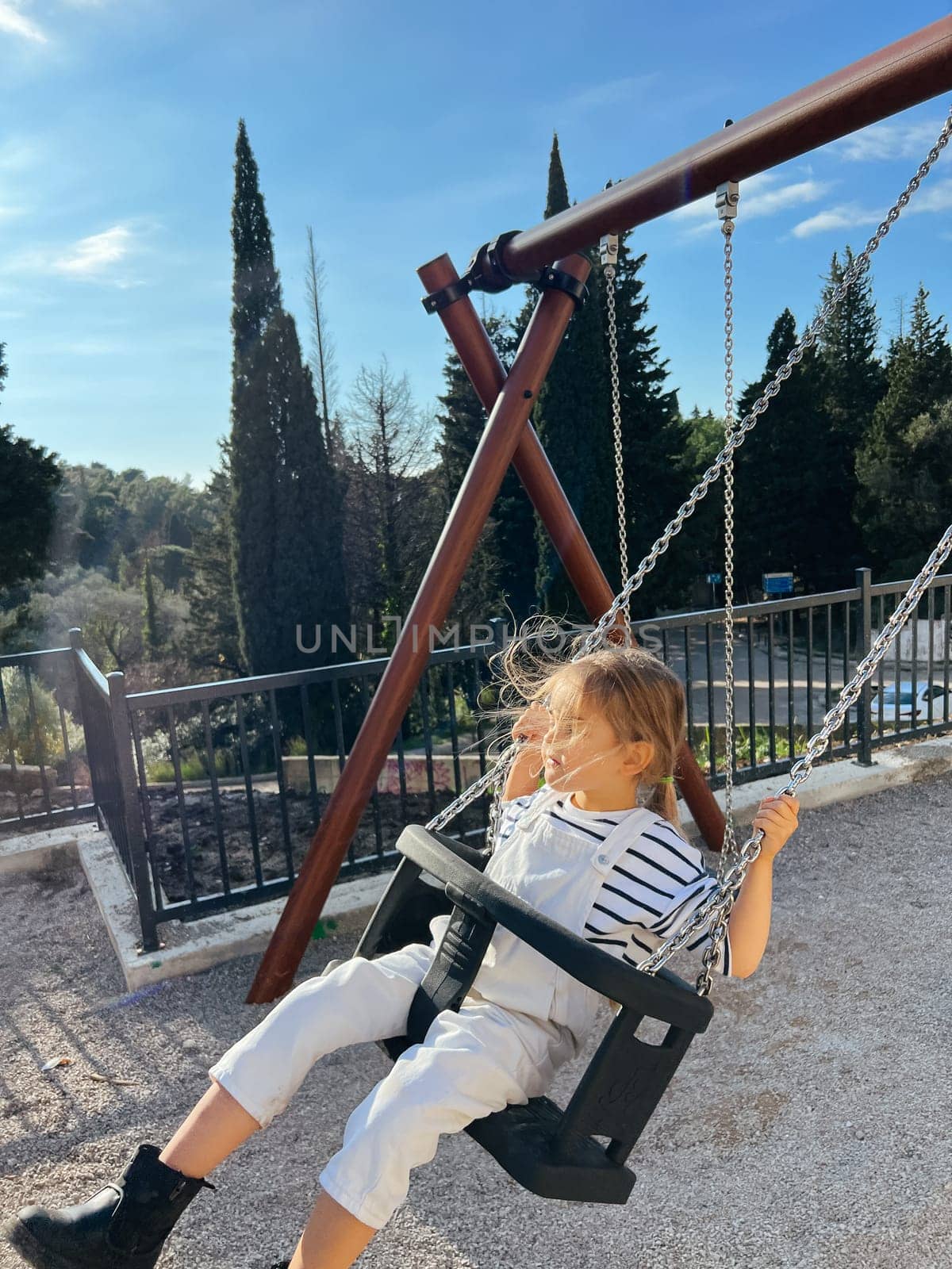 Little girl swings on a chain swing in the park with her eyes closed. High quality photo