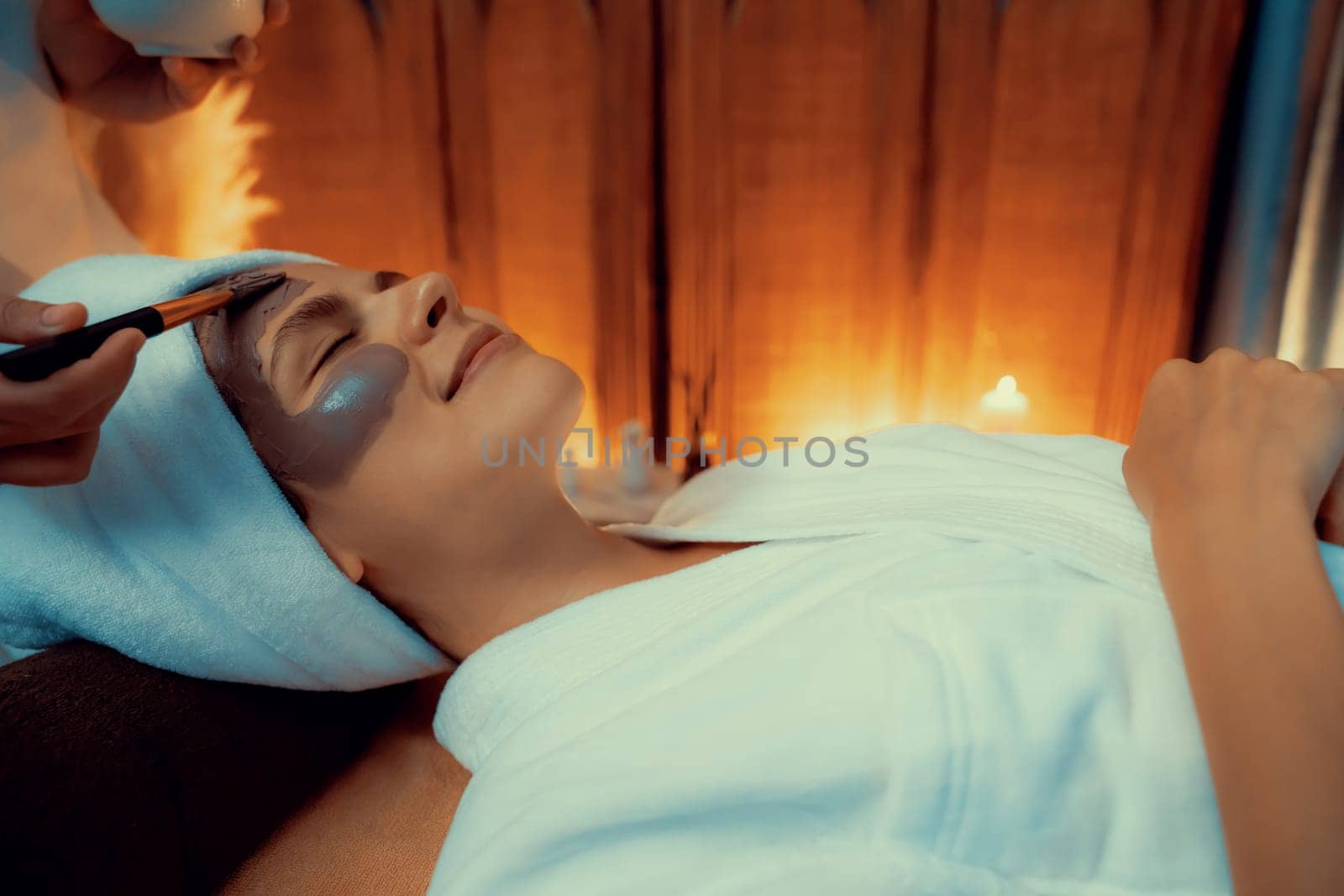 Serene ambiance of spa salon, woman customer indulges in rejuvenating with charcoal face cream massage with warm lighting candle. Facial skin treatment and beauty care concept. Quiescent