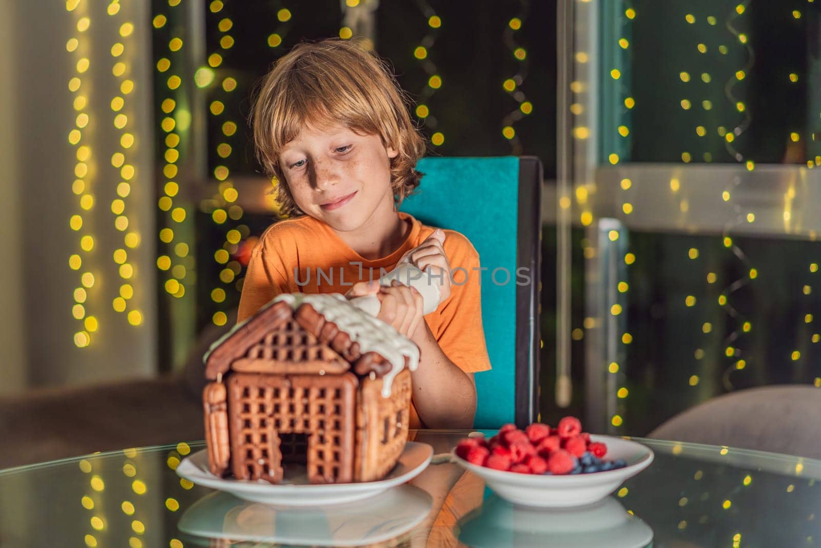 Immerse in festive delight as a boy crafts boy crafting an unconventional gingerbread house, infusing Christmas with unique creativity and festive cheer. A sweet scene of seasonal bonding and culinary fun by galitskaya