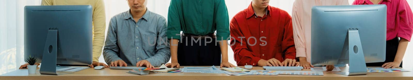 Young asian startup group works together on a project. Professional business people determine and focus on their performance while standing at office room with office equipment placed. Variegated.