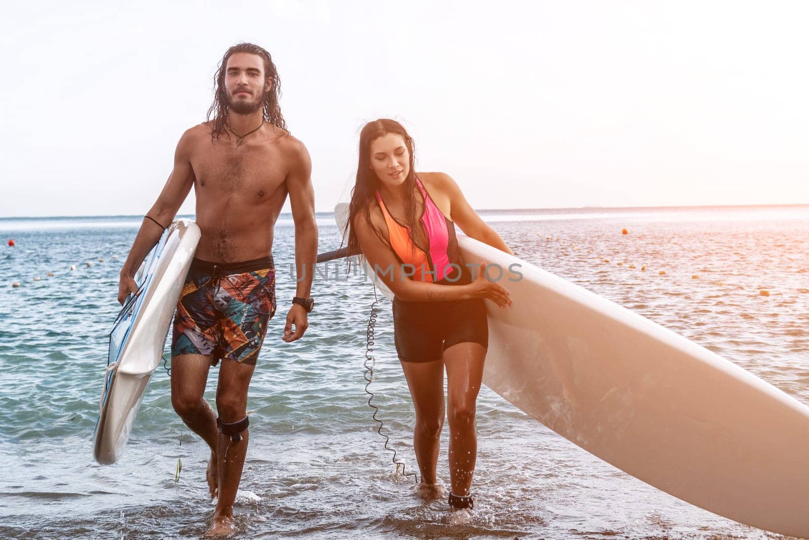 Sea woman and man on sup. Silhouette of happy young woman and man, surfing on SUP board, confident paddling through water surface. Idyllic sunset. Active lifestyle at sea or river
