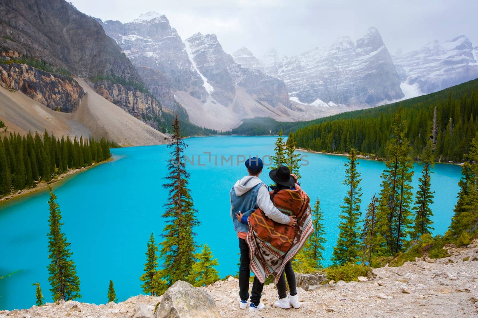 Lake Moraine during a cold snowy day in Canada, turquoise waters of Moraine Lake with snow at Banff National Park Canadian Rockies. Young couple men and women standing by a lake in Canada