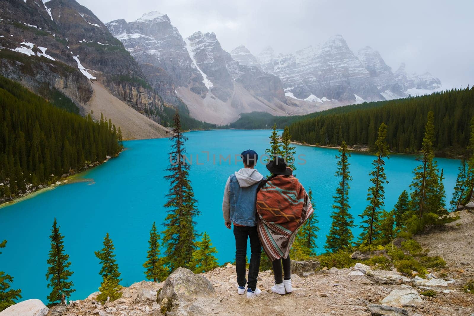 Lake Moraine during a cold snowy day in Canada, turquoise waters of Moraine Lake with snow at Banff National Park Canadian Rockies. Young couple men and women standing by a lake in Canada at sunrise