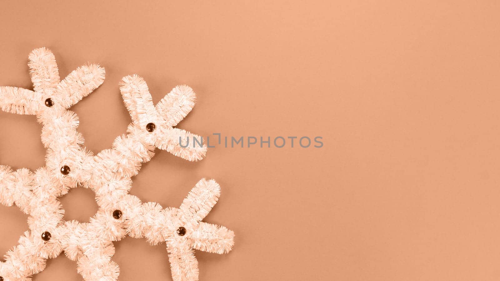 Fluffy white snowflake Christmas decor. Image toned in Peach Fuzz color of the year 2024. The concept of New Year and Christmas holidays, congratulations. Copy space. View from above.